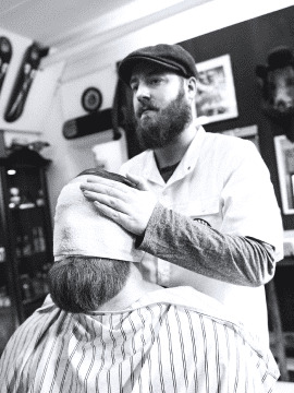 the barber applies a warm towel to the client's face